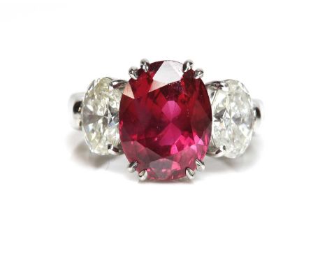 A three stone unheated ruby and diamond ring,with an oval mixed cut ruby double claw set to a plain collet, with a brilliant 