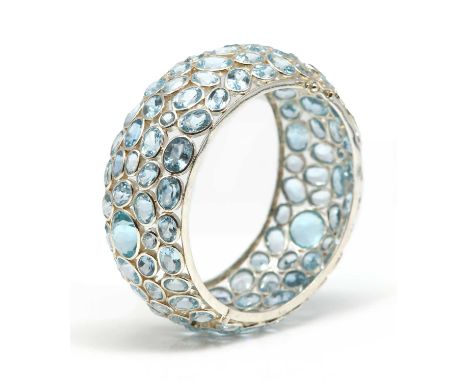 A sterling silver blue topaz hinged bangle,composed of graduated oval and circular mixed cut blue topaz, all individually rub