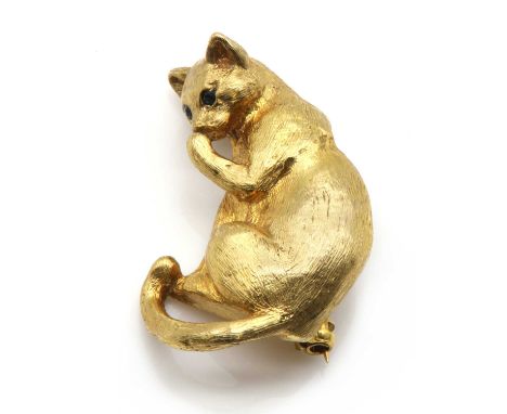 A 9ct gold cat brooch, by Harriet Glen,naturalistically modelled as a cat licking its paw, with round mixed cut sapphire set 