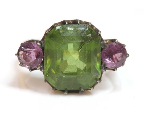 An Edwardian three stone peridot and pink sapphire ring,with a trap cut peridot, claw set to the centre, with a circular mixe