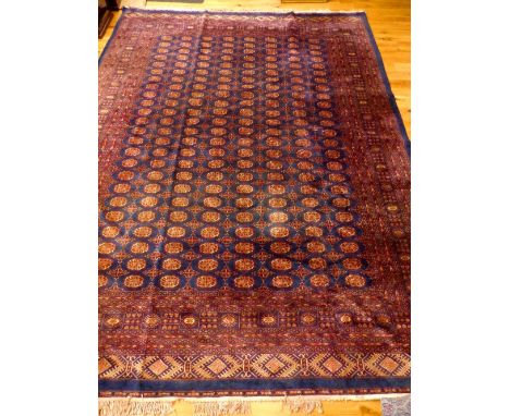 Bokhara carpet, decorated with red and cream elephant pad medallions over indigo ground, within geometric borders, 400x 282cm