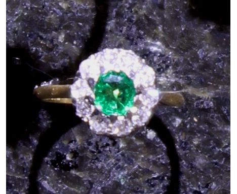 An emerald and diamond cluster ring in 18ct yellow gold and platinum, the central oval cut 0.63ct emerald surrounded by round