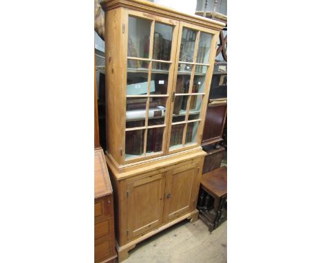 Small stripped pine bookcase, the moulded cornice above a pair of bar glazed doors, the base with two panel doors on bracket 