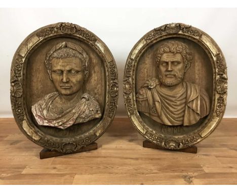 Pair of 20th century highly decorative carved wooden oval roundels depicting portrait busts of Roman Emperors, on display sta