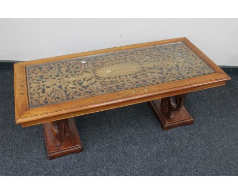 An eastern carved mahogany and brass inlaid coffee table with glass inset panel on elephant supports 