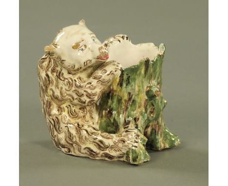 A Continental tin glazed model of a seated bear, 19th century, sat pawing at a tree trunk.