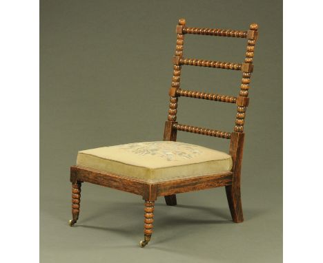 A 19th century simulated rosewood low chair, with upholstered seat and raised on bobbin turned legs with castors.  Width acro