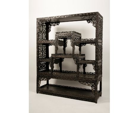 A CHINESE CARVED HARDWOOD DISPLAY STAND, late Qing dynasty, comprising eight tiered shelves, each with scroll and lotus pierc