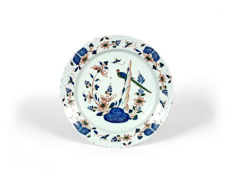 A delftware charger, c.1740, painted in red, blue and green with a long-tailed bird perched on tall rockwork above flowering 