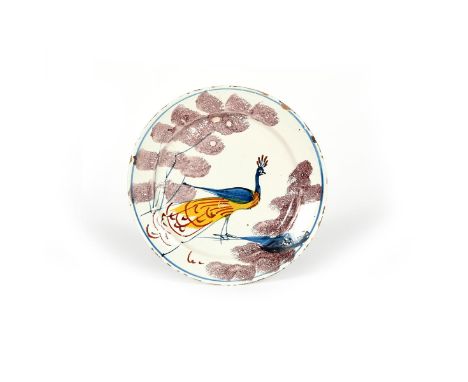 A Bristol delftware 'Farmhouse' plate, c.1720-30, painted with a bold peacock in yellow, blue and red, standing between spong