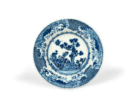 A Dublin delftware soup plate, c.1760, painted with a bird in flight above a pine tree encircled by an ornamental fence, a fu