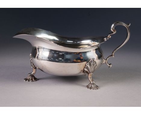 PRE-WAR SILVER SAUCE BOAT OF GEORGIAN DESIGN with everted cut rim and scroll handle, standing on three shell-capped scollop s