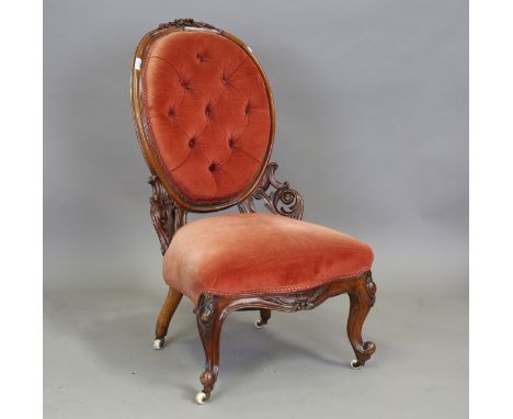 A Victorian mahogany carved showframe settee, upholstered in buttoned red fabric, raised on cabriole legs and ceramic castors