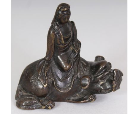 A GOOD CHINESE MING DYNASTY BRONZE SCROLL WEIGHT, cast in the form of Guanyin seated on the back of a Buddhistic lion, 2.75in