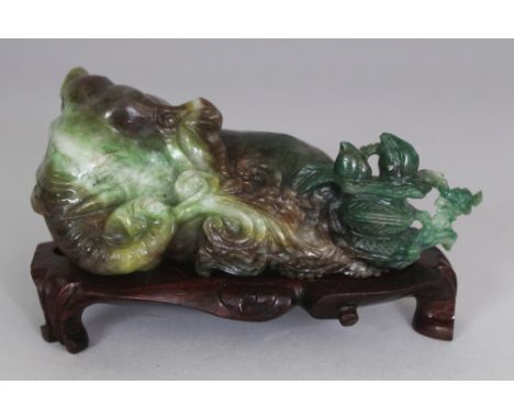 A CHINESE JADE MODEL OF A RECLINING ELEPHANT, together with a fitted wood stand, the elephant grasping a frond of lingzhi in 