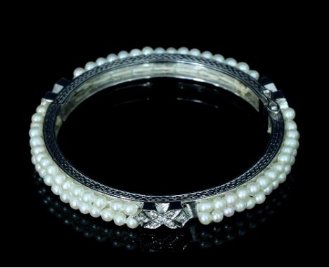 A diamond and pearl bangle, of hinged form, the two rows of pearls interspersed by three diamond set panels, one being the cl