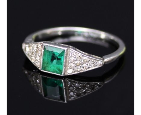 An Art Deco emerald and diamond ring, the central emerald with a triangular panel of pavé
 set diamonds to each shoulder on a