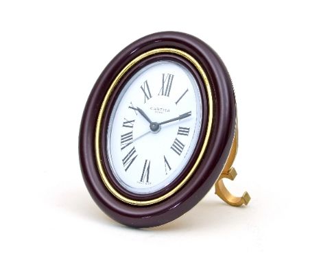 A Cartier alarm clock, the oval dial with Roman numerals within a burgundy enamel frame on an easel support, 9cm high and in 