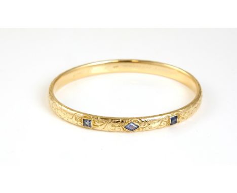 A gold bangle with engraved decoration and inset with three light blue sapphires, the interior engraved with latin inscriptio