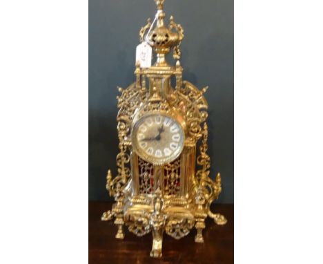 A contemporary brass quartz mantle clock, having pierced decoration throughout, the urn finial over circular dial on six supp