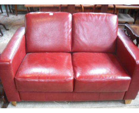 A contemporary two seater red leather sofa (141cm).