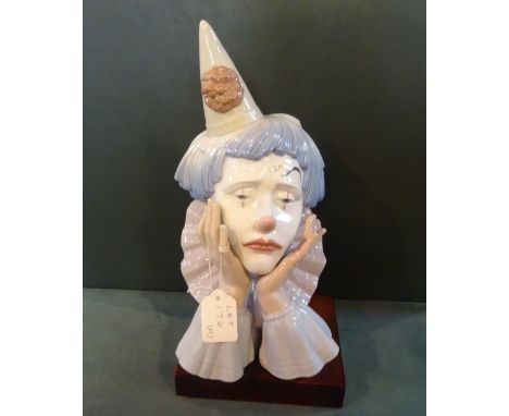 A Lladro clown head on wooden stand.