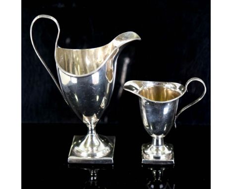 A George III silver helmet-shaped pedestal cream jug, hallmarks London 1792, height 18cm, and an Edwardian silver pedestal cr