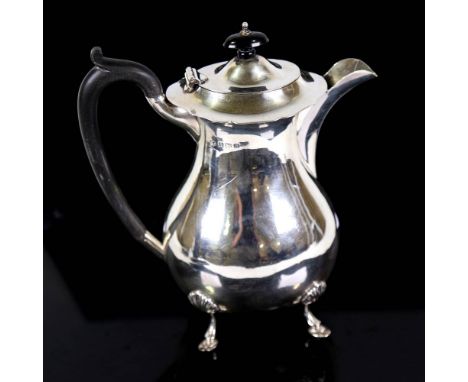 A George V silver hot water jug, oval bulbous form with scalloped rim, hoof feet and ebonised mounts, by S Blanckensee & Sons