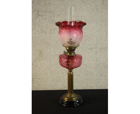 A Victorian paraffin oil lamp, with cranberry coloured reservoir, cranberry tinted acid etched shade on brass Corinthian flut
