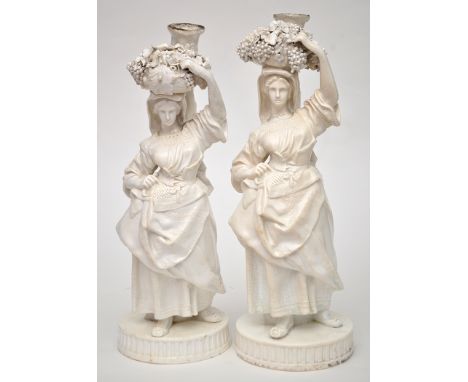 Pair of Derby (Stevenson and Hancock) candlestick figures of grape harvesters, modelled as female figures carrying a grape ba