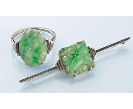 A carved jade ring, the plaque depicting scrolls flanked by stepped shoulders, on white metal shank stamped '9ct.', ring size