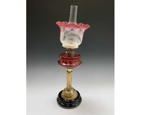 A Victorian brass oil lamp, with cranberry reservoir, on a column support and circular ceramic base, with frosted and cranber