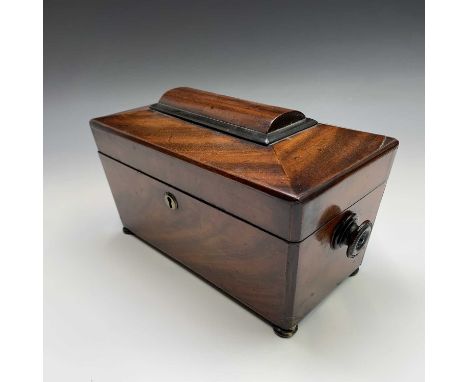 An early Victorian mahogany tea caddy of sarcophgus form, on bun feet, with fitted interior and glass liner. Height 18cm, wid