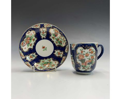 A Worcester scale blue ground cup and saucer, circa 1770, painted with polychrome floral panels within rococo gilt edge borde