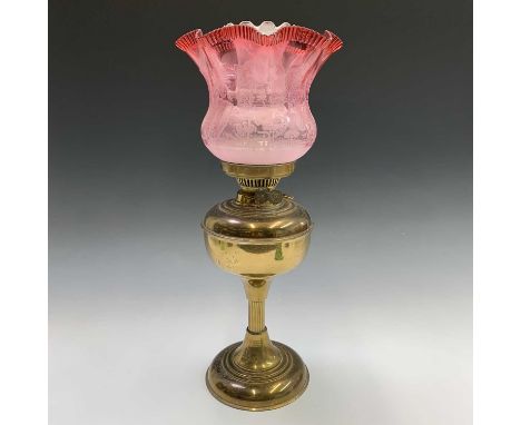 A late19th/early 20th century brass oil lamp, the frilled cranberry glass shade etched with floral decoration. Height 50.5cm.