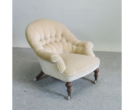 A cream upholstered button back armchair, standing on turned legs and castors