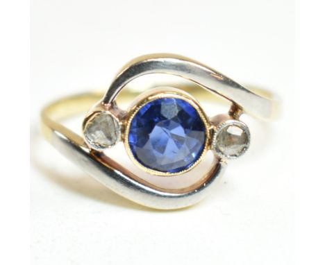 An 18ct gold, sapphire and diamond cross over ring. The ring having a central bezel set sapphire with a millegrain border fla