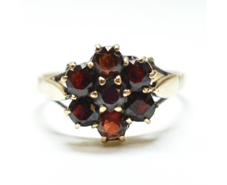 A hallmarked 9ct gold and garnet cluster ring. The ring having central six claw set round cut garnet surrounded by a halo of 