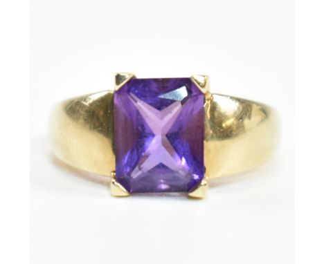 A hallmarked 9ct gold and amethyst ring. The ring set with a central emerald cut amethyst in a domed band ring to tapered sha