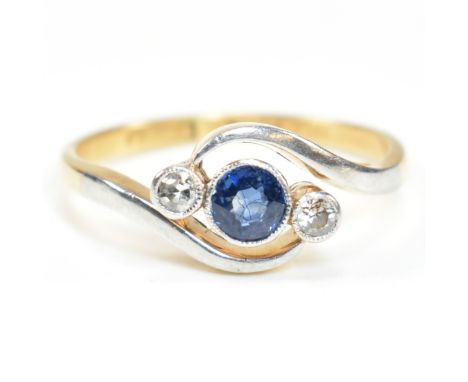 An 18ct gold, diamond and sapphire crossover ring. The ring having a central bezel set round cut diamond with millegrain bord