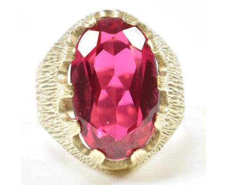 A 1970s 14ct gold and synthetic ruby ring. The ring having a large claw mounted oval mixed cut synthetic ruby to textured bar