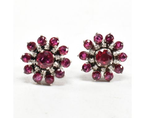 A pair of white gold ruby and diamond cluster earrings. The earrings set set with round cut rubies and single cut diamonds to