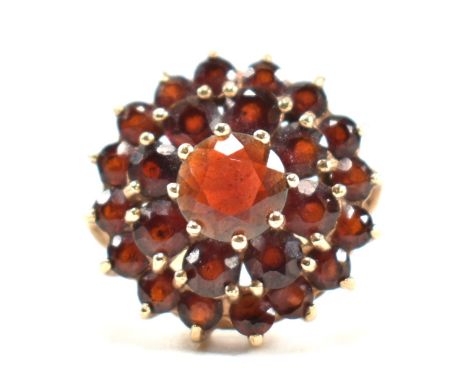 A hallmarked 9ct gold and garnet cluster ring. The ring set with a central round cut garnet surrounded by two halos of round 