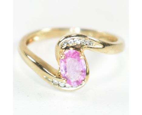 A hallmarked 9ct gold, pink sapphire and diamond crossover ring. The ring set with a central four claw set oval cut pink sapp