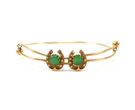 A Chinese gold and jade bangle. The bangle formed with two horseshoe motifs set with central jade cabochons to  expanding wir