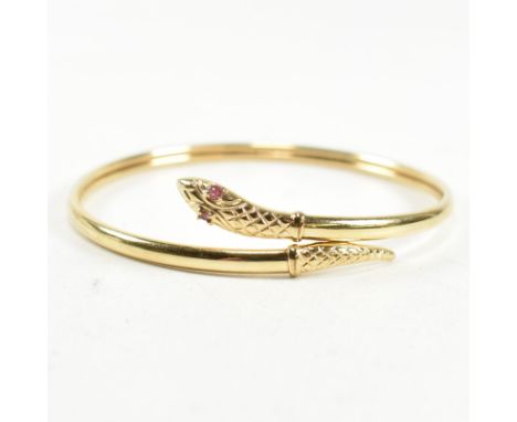 A 9ct gold and ruby snake bangle. The snake bangle having a wrap-around design with the snake head and tail having an engrave