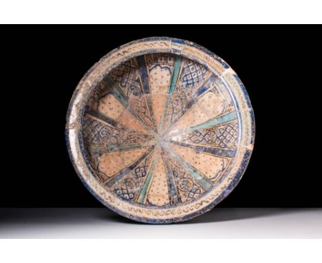 Ca. AD 1200 - 1300.
A Kashan painted bowl of deep rounded form atop a narrow foot, painted in cobalt blue, turquoise, and bla