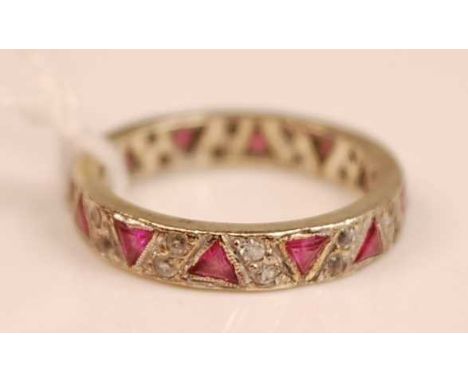 A white metal, ruby and white stone set full eternity ring, arranged as sunken triform rubies each dispersed with twin white 