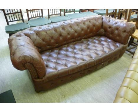 A three seater Chesterfield, having a level back, the brown hide button upholstered back, arms and seat raised on block legs 