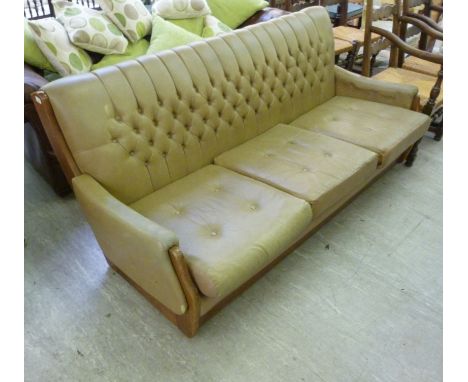 A 1960s teak finished, showwood framed settee, having a level back and low, enclosed arms, button upholstered in cafe-au-lait